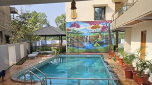 A swimming pool with a mural, surrounded by potted plants and a gazebo. - Shrikar Resort (Nagaon)