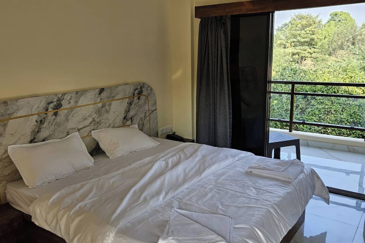 A bedroom with a marble headboard, white bedding, a view of greenery through a window, and an air conditioning unit above the window.