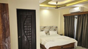 A modern bedroom with a marble headboard, a large bed, a ceiling fan, and a door with a unique design. - Shrikar Resort (Nagaon)