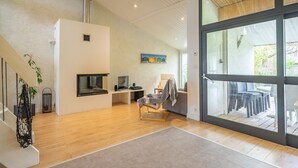 A modern interior with a wooden floor, a fireplace, a dining area with outdoor seating, and a large glass door leading outside. - Spacious Villa 10 min from Royan – 4 Bedrooms, Garden, Terrace, Ideal for Families and Friends (Saujon)