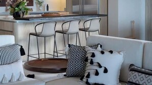 Een moderne keuken met een centraal eiland, roestvrijstalen apparatuur en een zithoek met een bank en stoelen.