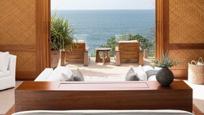A bedroom with a large bed, a wooden coffee table, two armchairs, and a view of the sea.