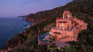 Una villa de piedra con piscina, situada en una colina con vistas al mar.