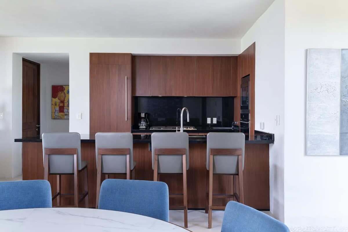 Een moderne keuken met houten kastjes, een zwart aanrecht en een centraal kookeiland met barstoelen.