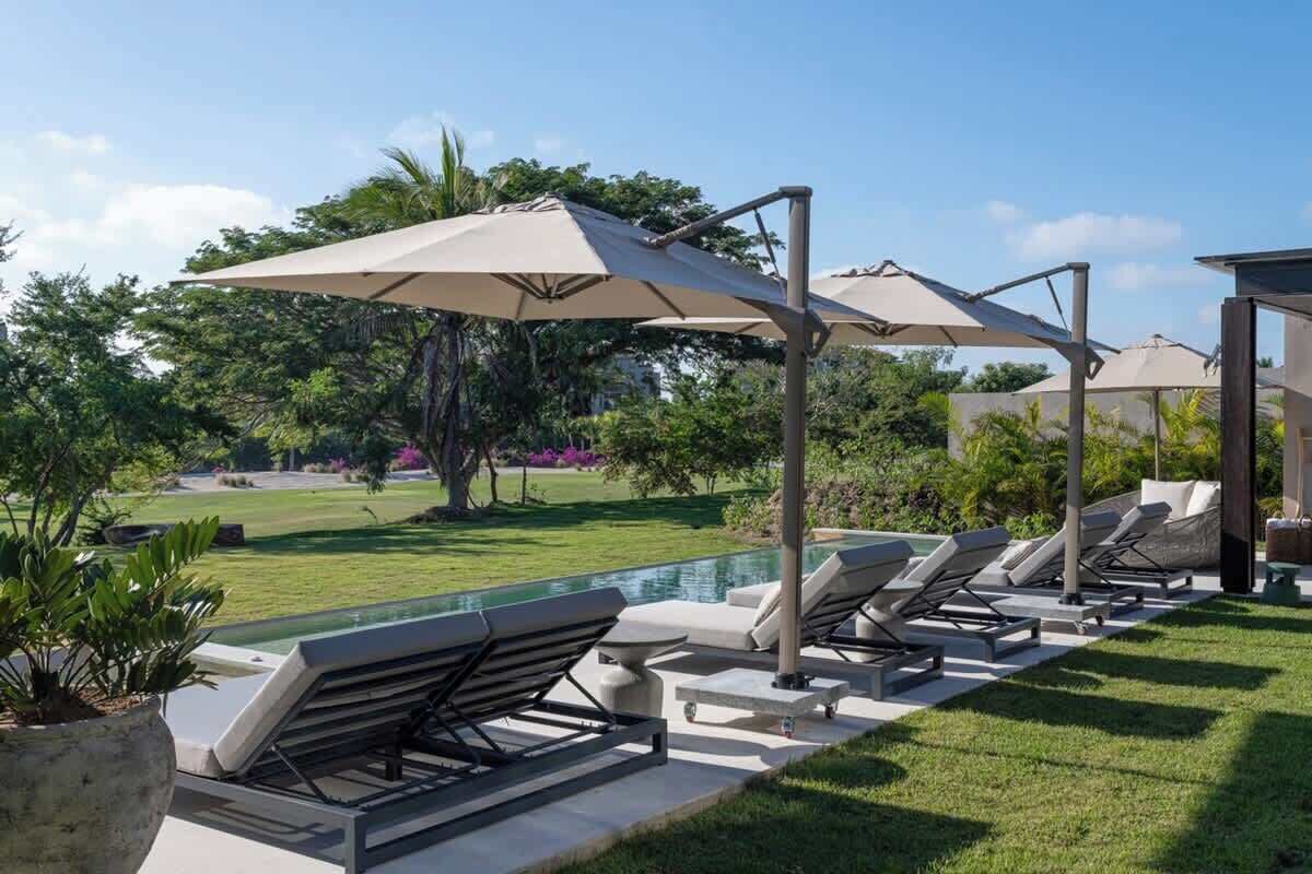 A poolside area with lounge chairs and umbrellas, surrounded by a well-maintained lawn and trees.