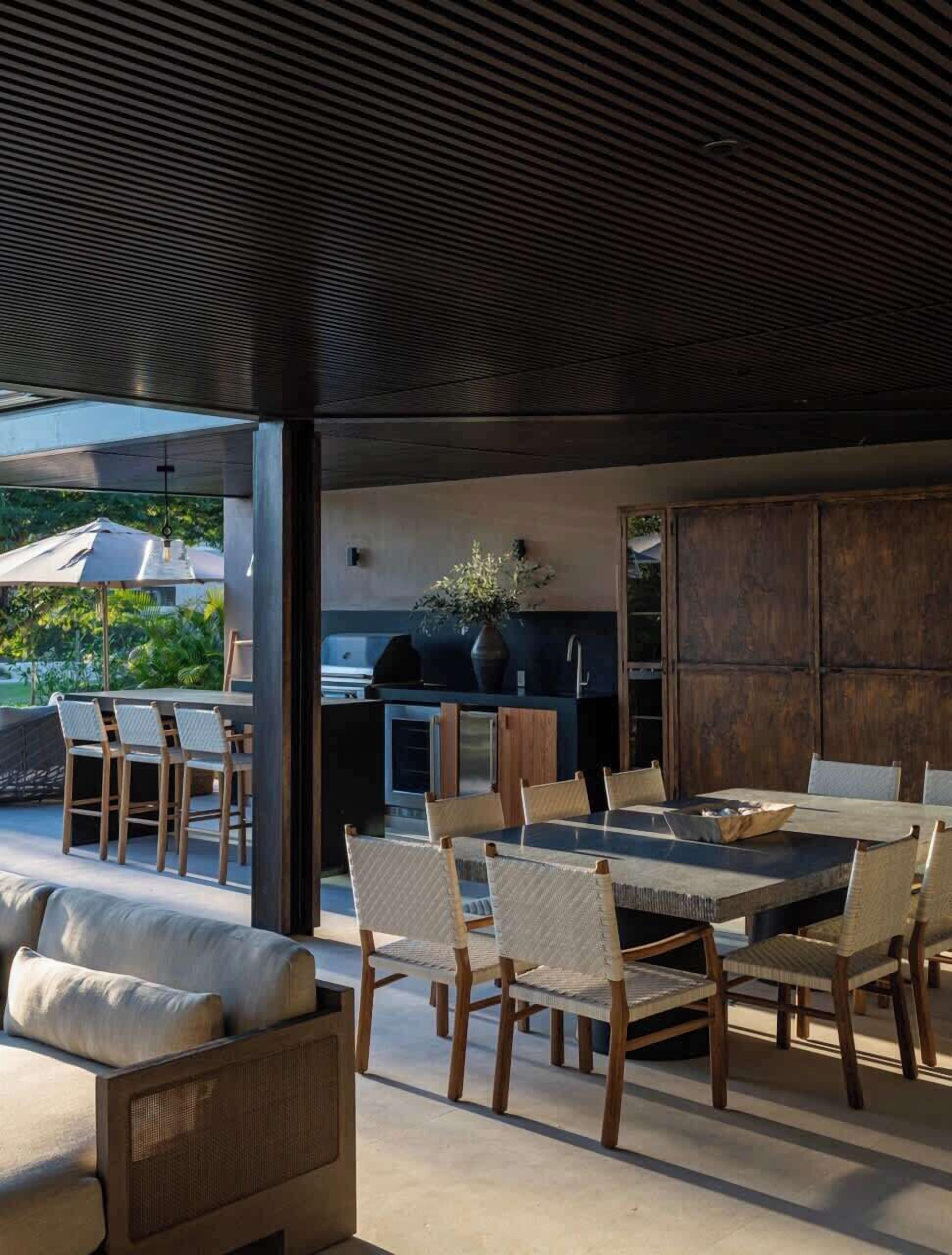 Un área de comedor al aire libre con diseño moderno, que incluye una mesa grande, sillas, una parrilla y vistas del paisaje circundante.