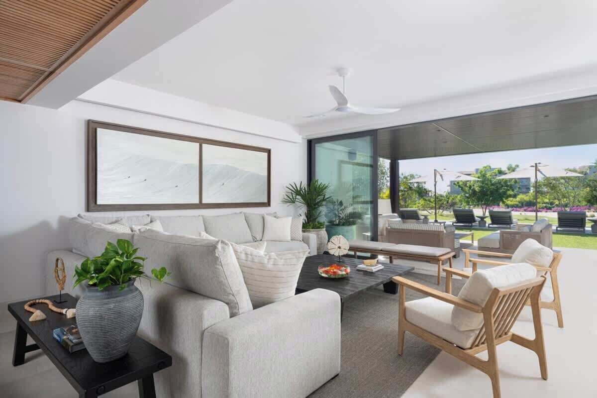 A modern living room with a sofa, coffee table, and chairs, large windows, and a ceiling fan.