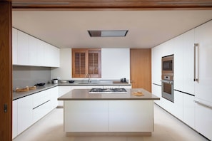 Una cocina moderna con armarios blancos, una isla central, horno empotrado y una ventana con contraventanas de madera.