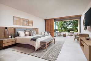 Un dormitorio moderno con una cama grande, mesitas de noche, un banco y vistas al exterior a través de un ventanal.