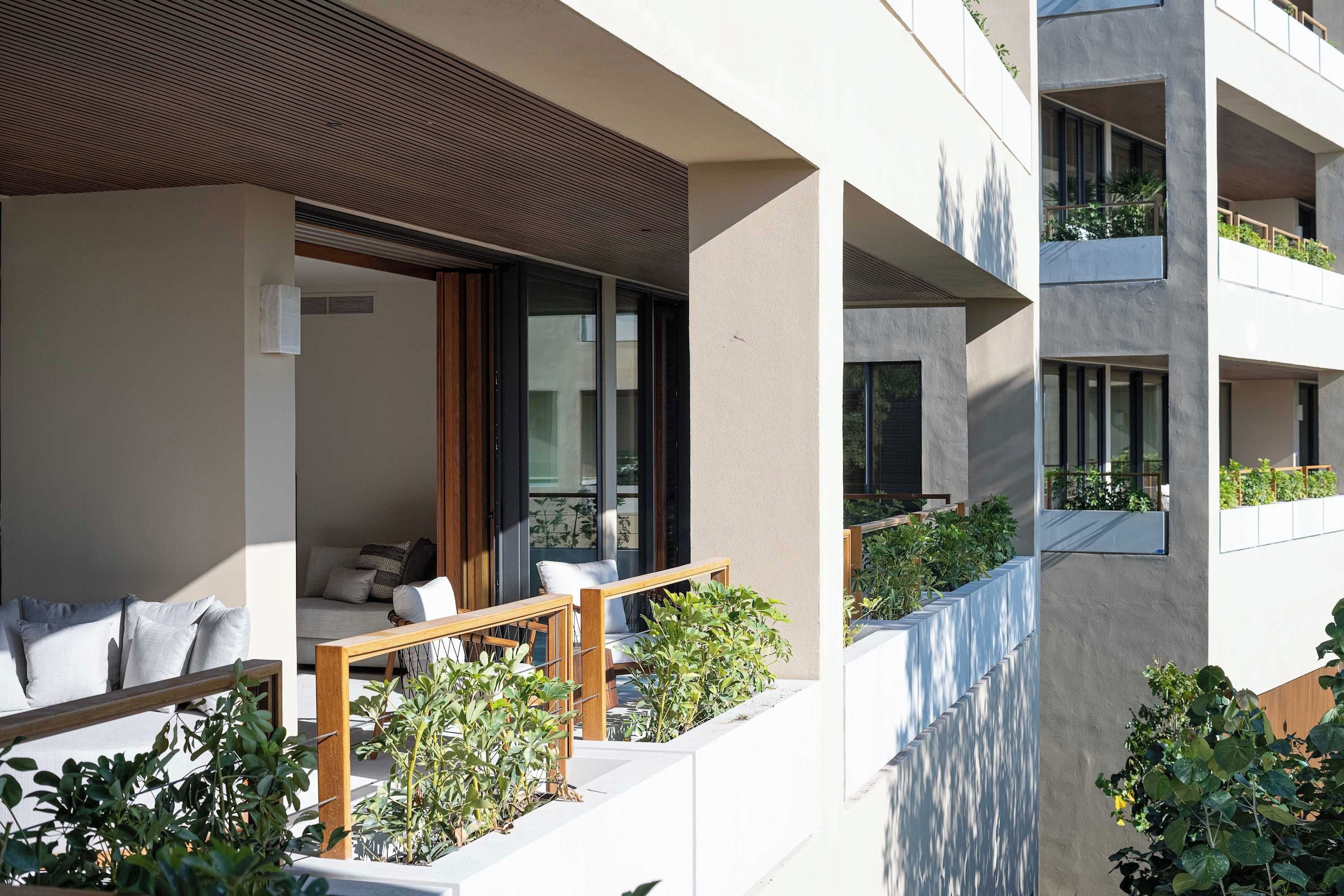 Un edificio moderno con balcón, mobiliario exterior y vegetación.