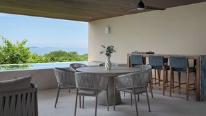 Un área de comedor al aire libre con vista al mar, una mesa redonda y sillas de mimbre.