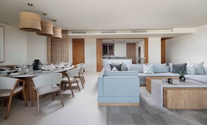 Ein modernes Wohnzimmer mit einem grauen Sofa, einem Esstisch für vier Personen und einer Küche im Hintergrund.