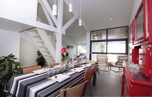 A dining area with a long table set for a meal, a staircase, and a red appliance on the right. - Escape to a Villa in Saujon – 170 m², Garden, Close to Beaches & Vineyards, Ideal for 9 People (Saujon)