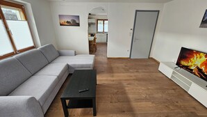A living room with a grey sectional sofa, a black coffee table, and a TV displaying a fireplace. - FeWo in der Kiese Hard - Top 2 "Bodensee" with a large terrace (Hard)
