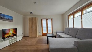 A modern living room with a grey sofa, a flat-screen TV, wooden flooring, and a sliding door. - FeWo in der Kiese Hard - Top 2 "Bodensee" with a large terrace (Hard)