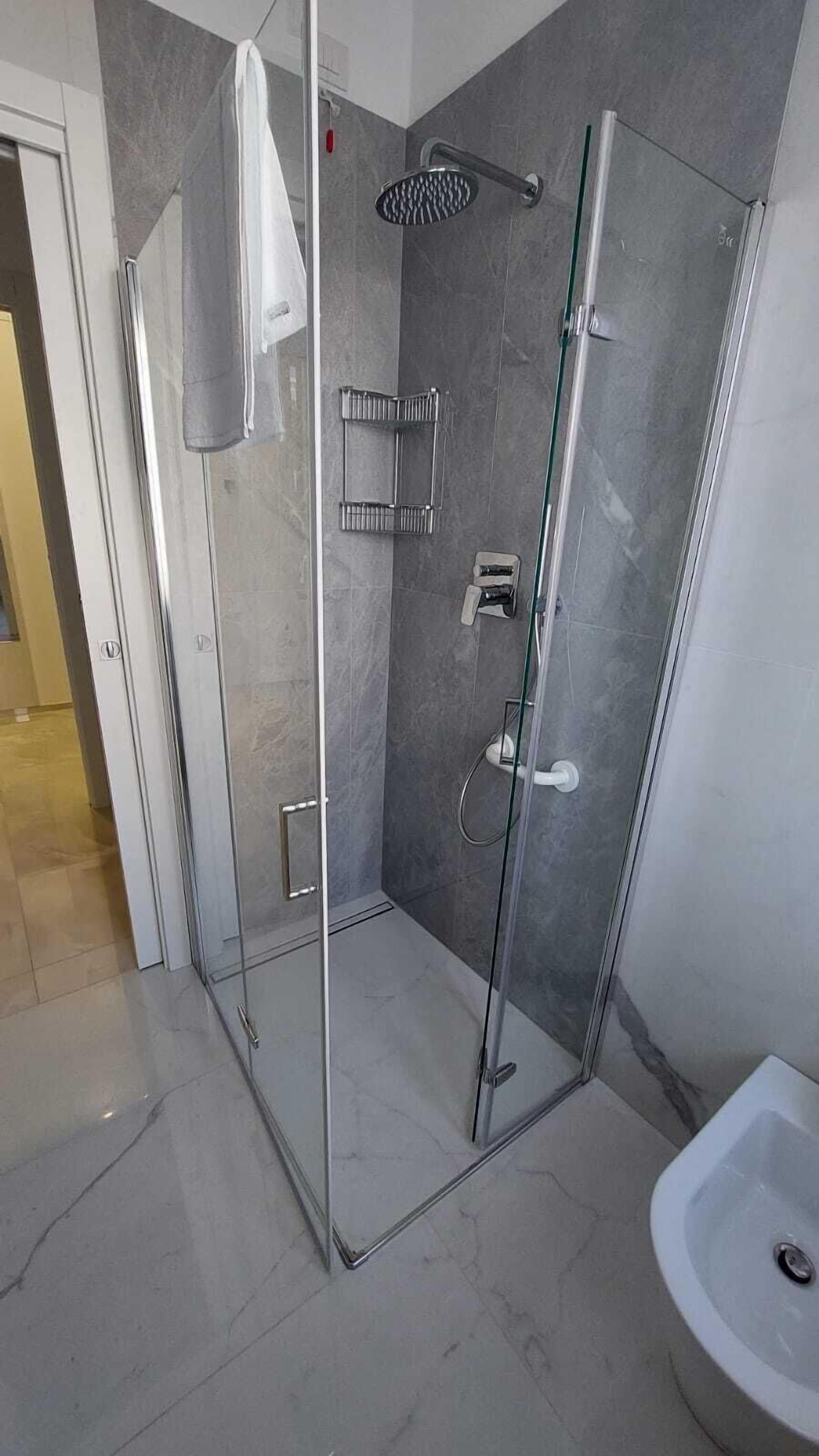 Ein modernes Badezimmer mit einer Duschkabine, einem weißen Waschbecken und einer Glastür zur Dusche.