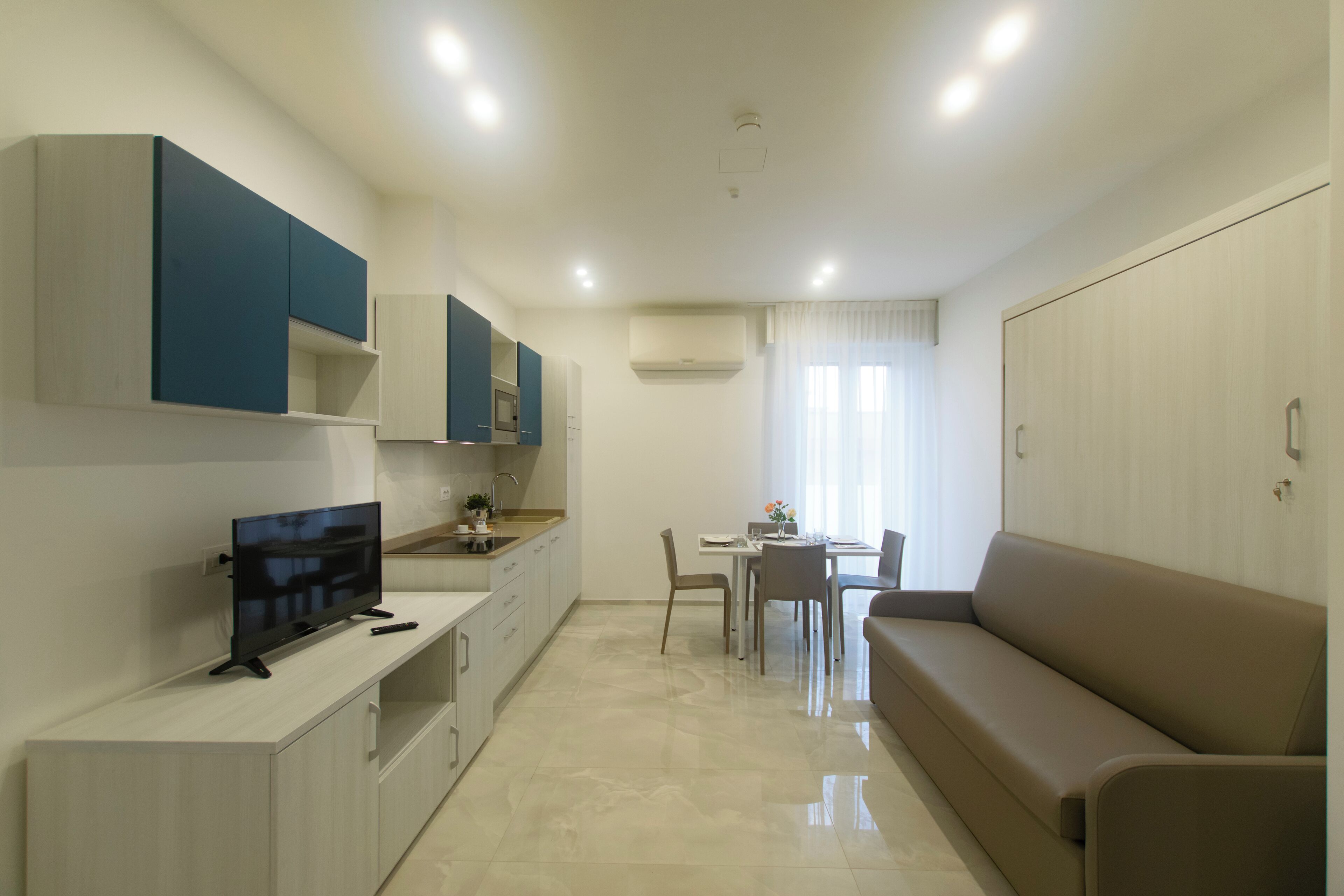 A modern kitchen with built-in appliances, a dining area with a table and chairs, and a sofa in a living area.