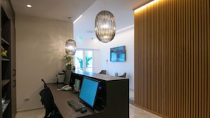 A modern reception desk with a computer, a telephone, and a potted plant. There is a wooden panel wall and a painting on the wall. - Residence Flow-r (Riccione)