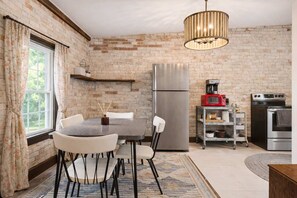 A kitchen with a brick wall, a stainless steel refrigerator, a microwave, a stove, and a dining table with chairs.