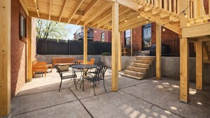 Un patio cubierto con terraza de madera, mobiliario exterior y una escalera que lleva a un nivel superior.