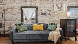 Una habitación con un sofá gris, cojines estampados, un aparador de madera y una pared de ladrillo.