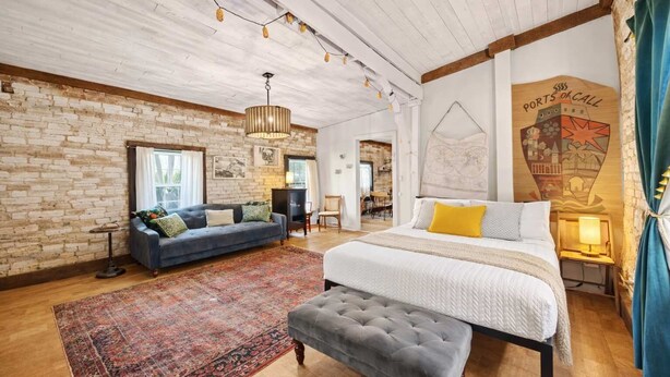 Habitación amplia con una cama grande, un sofá y un banco. Se aprecia una pared de ladrillo y un techo de madera.
