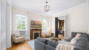 A spacious living room with a grey sofa, a fireplace, and a large window. - Classic & elegant Victorian home in Old Louisville (Louisville)