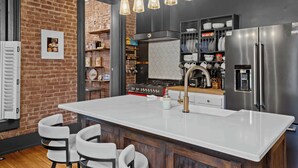 A modern kitchen with a large island, stainless steel appliances, and a brick wall. - Classic & elegant Victorian home in Old Louisville (Louisville)