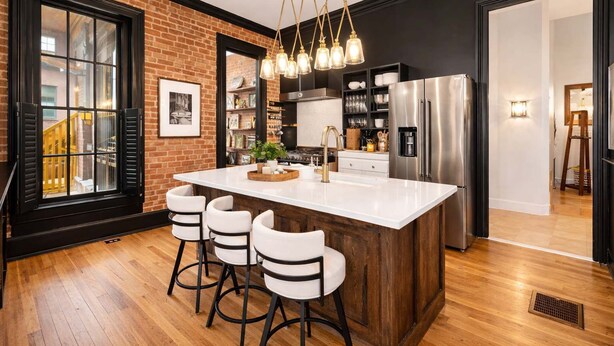 A modern kitchen with a large island, bar stools, a stainless steel refrigerator, and a brick wall. - Classic & elegant Victorian home in Old Louisville (Louisville)