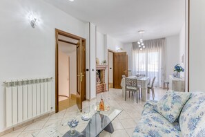 Un soggiorno con tavolino in vetro, divano a motivi floreali, zona pranzo con tavolo e sedie e camino.