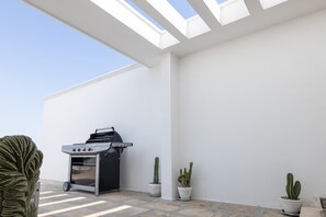 Une terrasse avec un barbecue, des cactus en pot et un ciel dégagé.