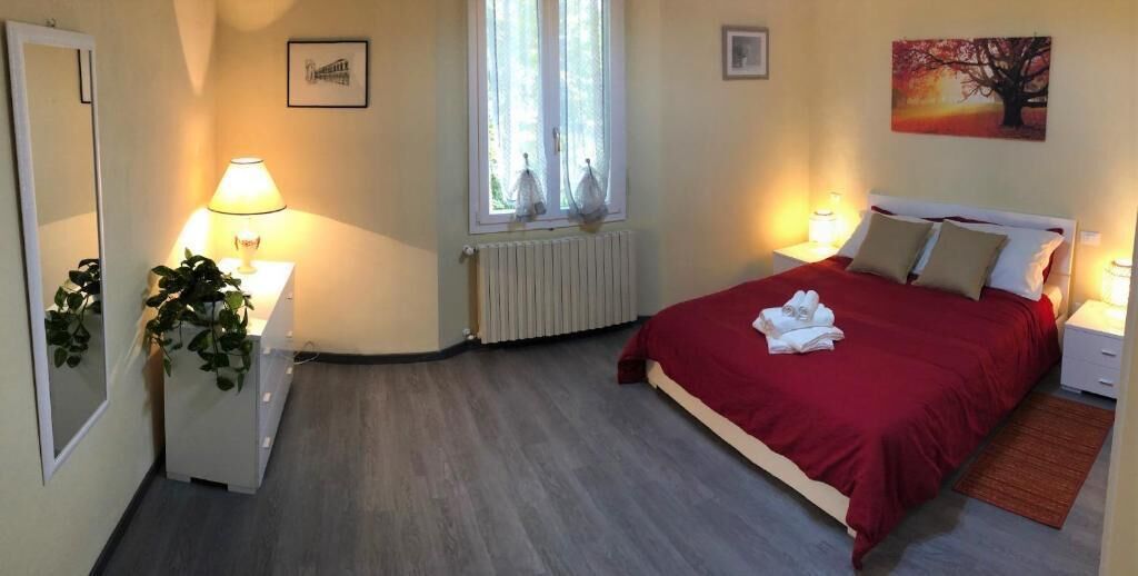 Une chambre à coucher comprenant un lit, des lampes de chevet, un radiateur, une fenêtre avec des stores, un miroir et une plante.
