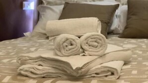 Un lit avec des serviettes enroulées et un livre, une couvre-lit à motifs et une tête de lit dotée d’un luminaire.