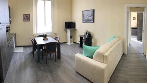 Un espace de vie compact comprenant un coin repas, un canapé, un téléviseur et un couloir menant à une autre pièce.