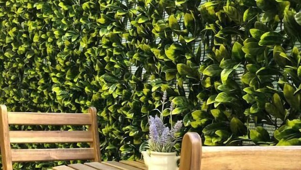 Un banc en bois avec une table devant une haie verte.