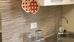 Une cuisine moderne dotée d’un évier en acier inoxydable, d’une plaque de cuisson à induction noire et de bocaux en verre transparent posés sur le plan de travail.