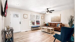 A living room with a brown leather couch, a blue armchair, a wooden coffee table, and a ceiling fan. - Cozy 3BR dog-friendly home just 13 min from Fort Campbell. Sleeps 6 with fast WiFi, a full kitchen, smart TVs and convenient access to APSU/F&M Bank Arena. (Clarksville)