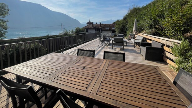 En træterrasse med udendørs møbler, med udsigt over vand og bjerge.
