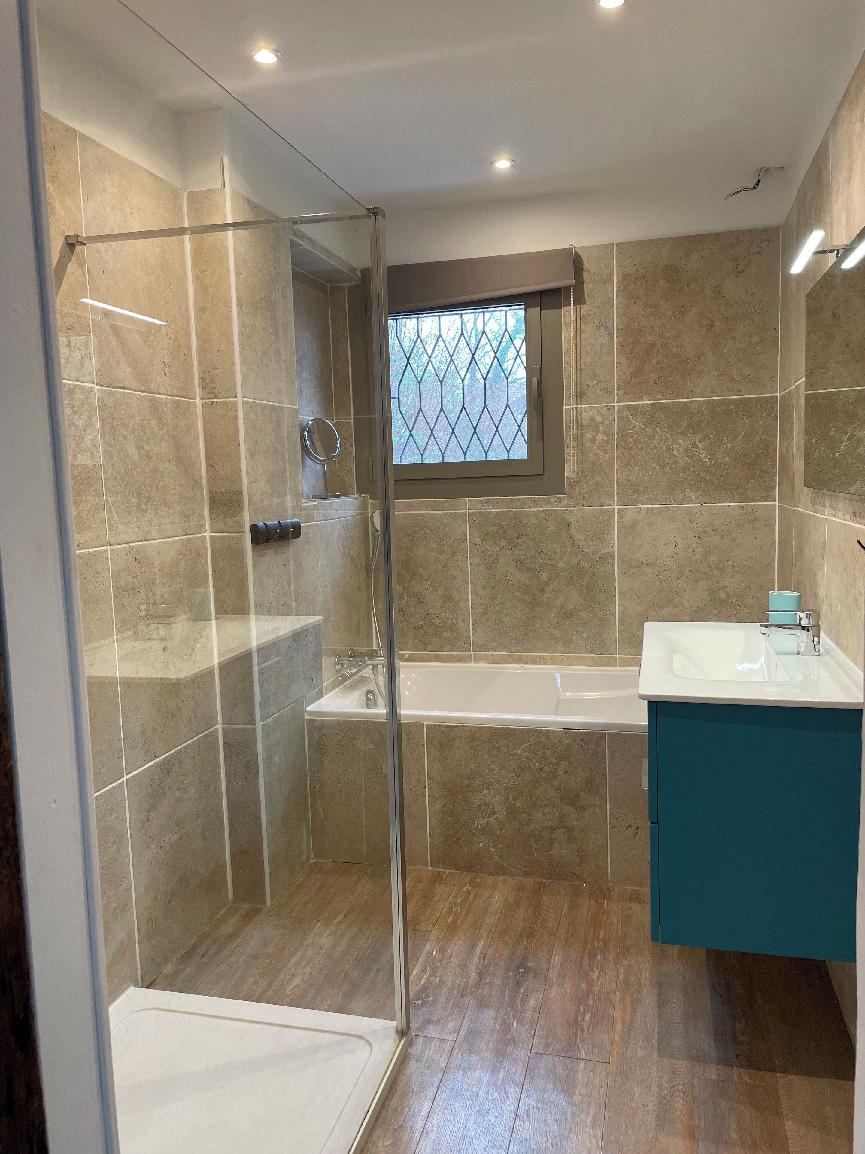 Een moderne badkamer met een douche met glazen wand, een badkuip en een wastafel met een blauwgroen kastje.