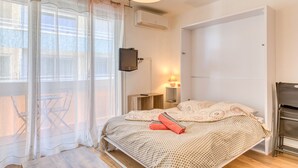 A bedroom with a bed, a TV, a bedside table, a lamp, and a window with curtains. - Studio direct access to the beach with sea view, Wi-Fi and air conditioning (Palavas-les-Flots)