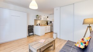A modern apartment with a kitchen, dining area, and a sofa with a colorful pillow. - Studio direct access to the beach with sea view, Wi-Fi and air conditioning (Palavas-les-Flots)