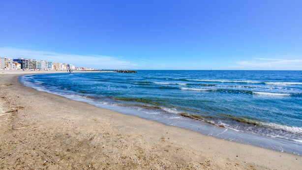 A beach with clear blue water, a sandy shore, and buildings in the background. - Studio direct access to the beach with sea view, Wi-Fi and air conditioning (Palavas-les-Flots)