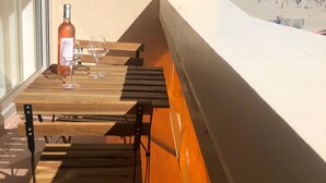 A balcony with a table, two chairs, a bottle, and two wine glasses. - Studio direct access to the beach with sea view, Wi-Fi and air conditioning (Palavas-les-Flots)