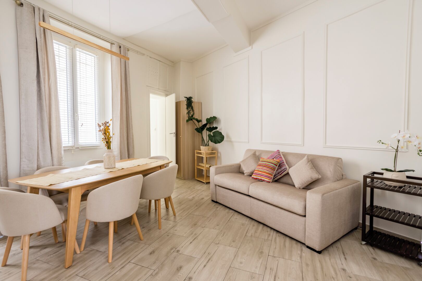 Un salon moderne avec un canapé beige, une table à manger en bois et une étagère en métal noir.