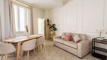 Un salon moderne avec un canapé beige, une table à manger en bois et une étagère en métal noir.