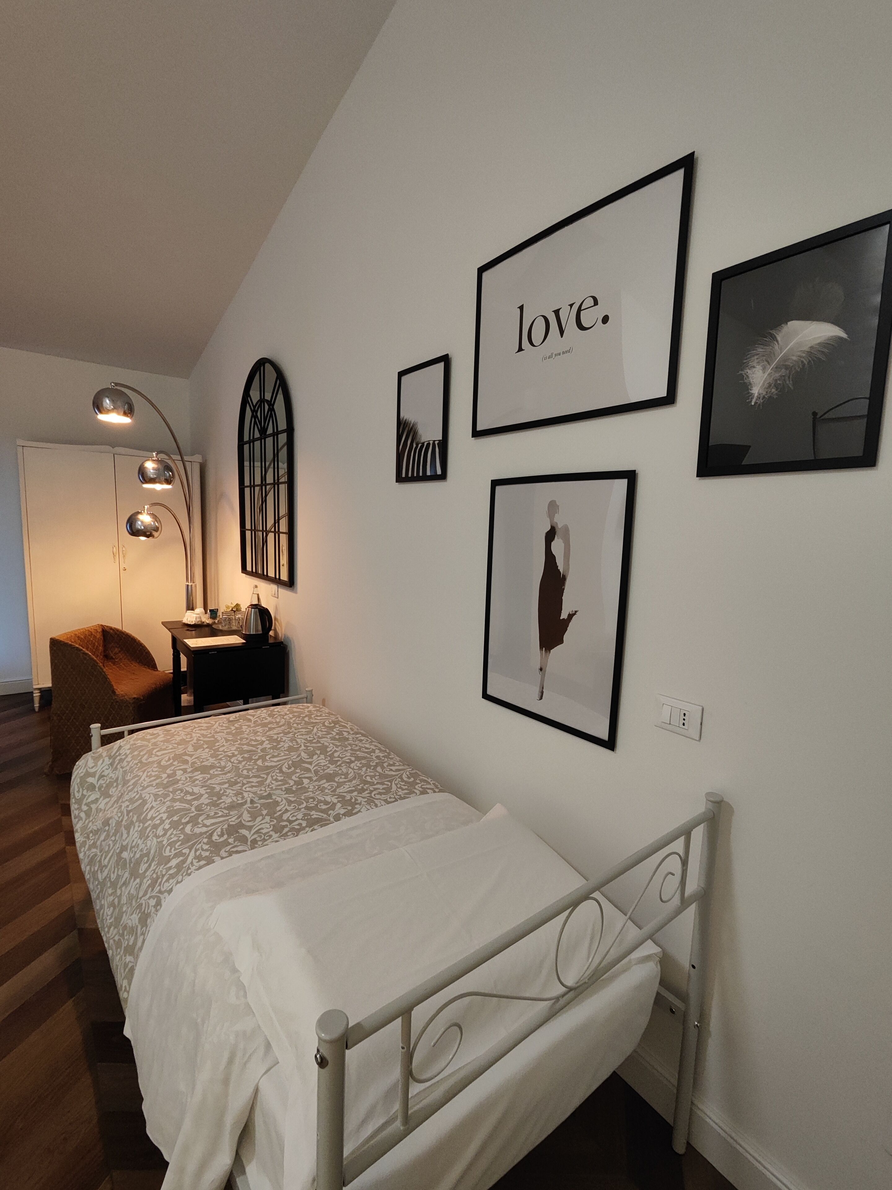 Une chambre bien rangée, avec un lit, un bureau et une chaise. Des tableaux encadrés ornent le mur, dont un sur lequel figure le mot « amour ».