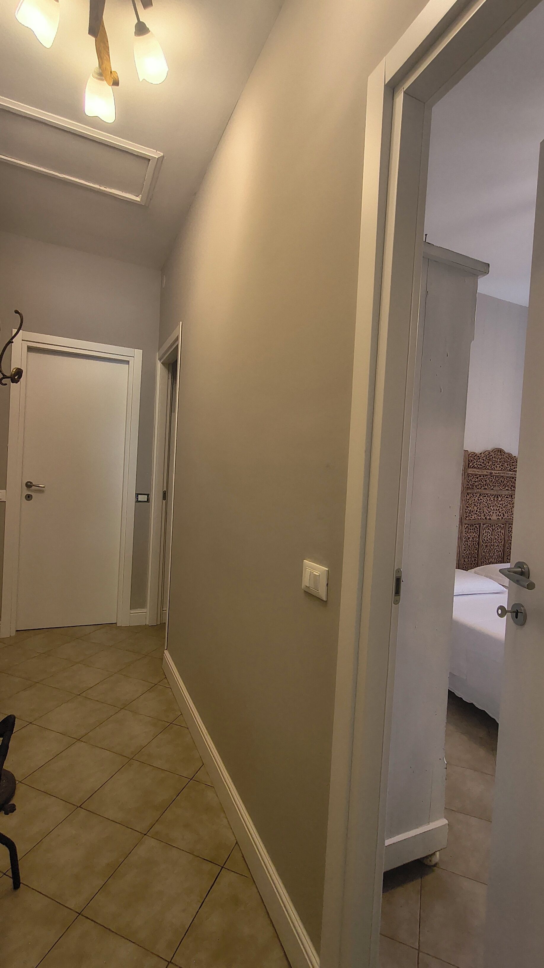 Un pasillo con una puerta que da a un dormitorio, una lámpara y una silla.