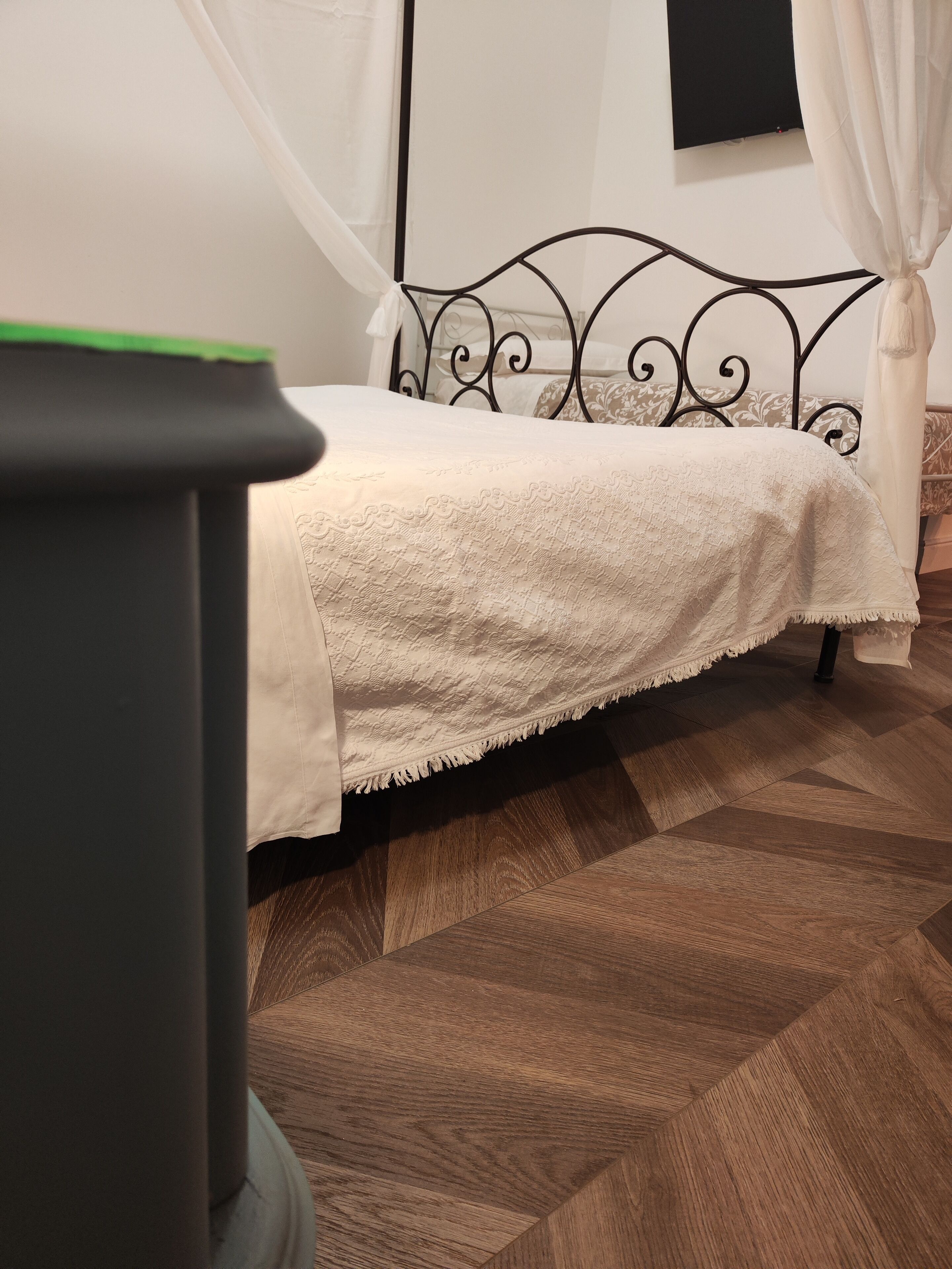A bed with a white blanket, a black metal headboard, and a wooden floor.