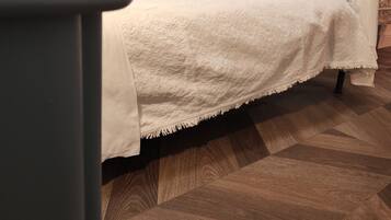 A bed with a white blanket, a black metal headboard, and a wooden floor.