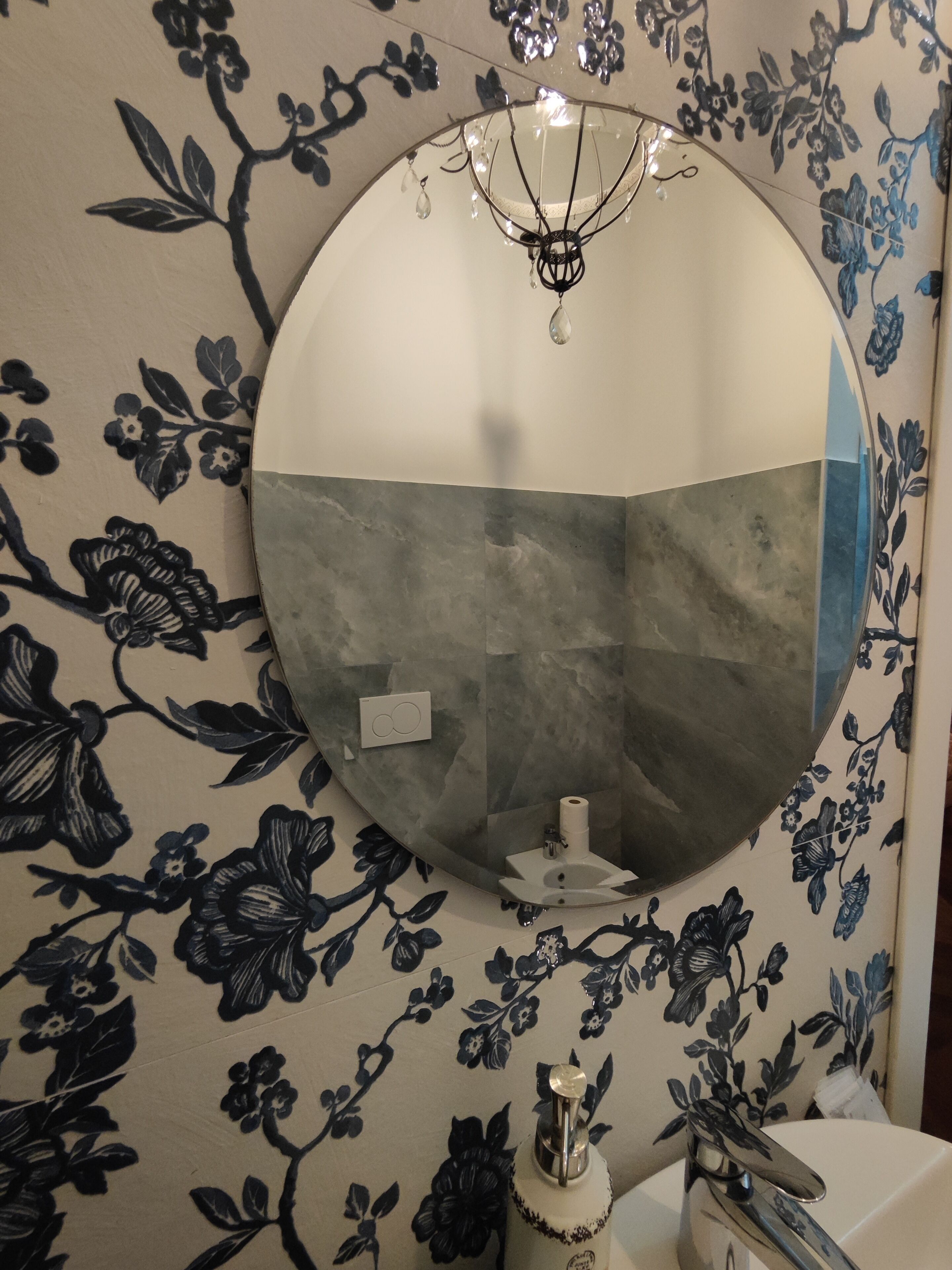 A bathroom with a round mirror, floral wallpaper, a sink, and a chandelier.